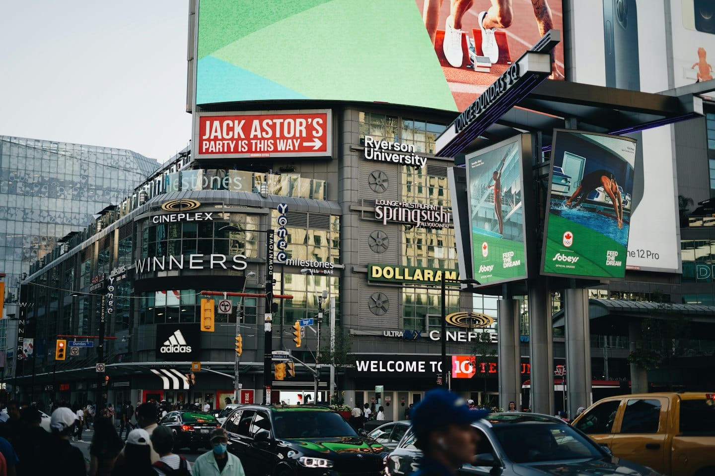 Crowds walk along a busy city street lined with retail stores.