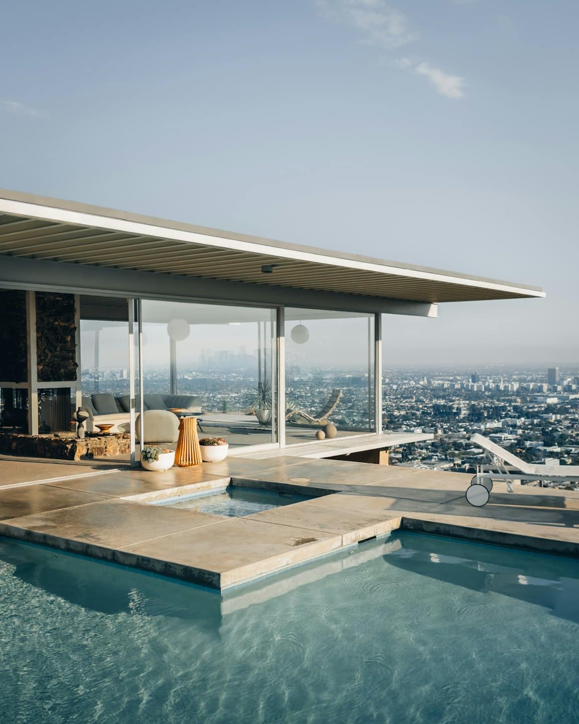 Modern house with glass walls and infinity pool overlooking city.