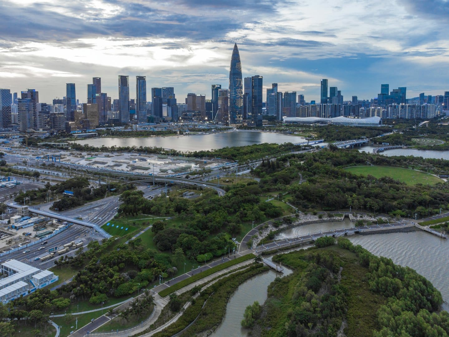 Modern city skyscrapers rise above green parks and winding waterways.